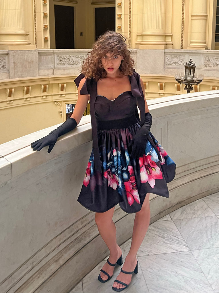 Woman in a floral dress with black gloves standing in an elegant interior setting